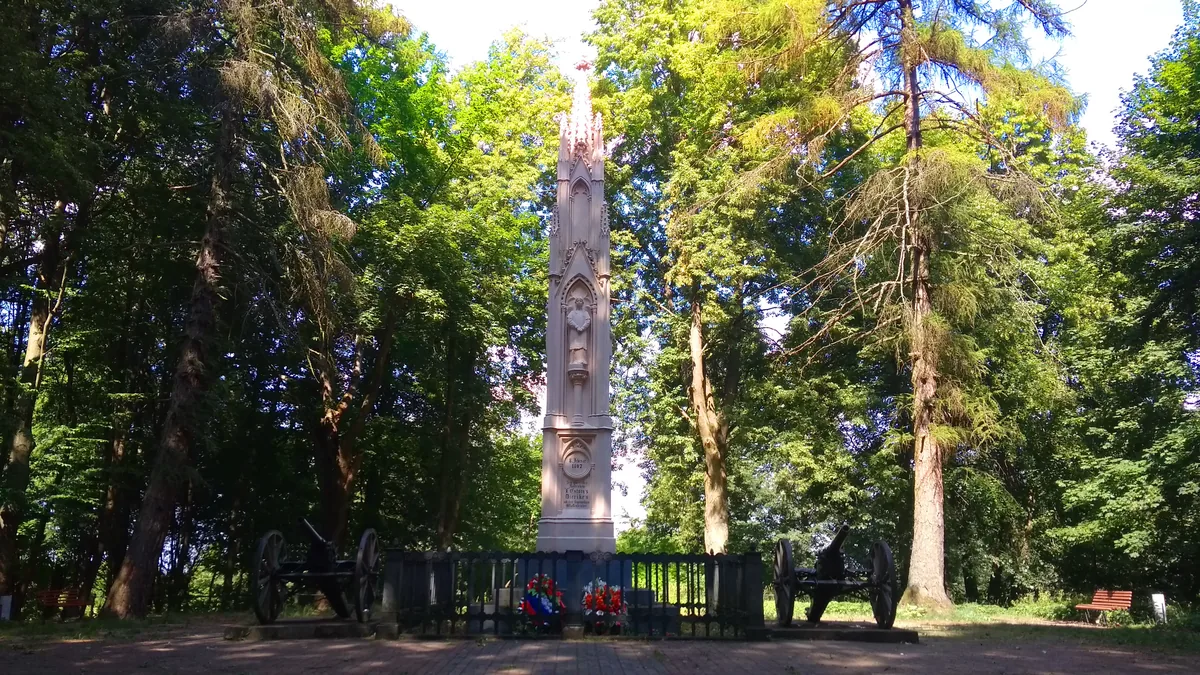 Pale stone obelisk at the end of a grassy avenue lined with tall trees