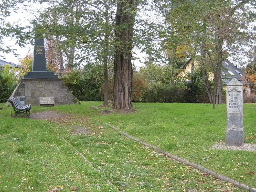 Obelisco nero su uno zoccolo di pietre, in un prato bordato di alberi