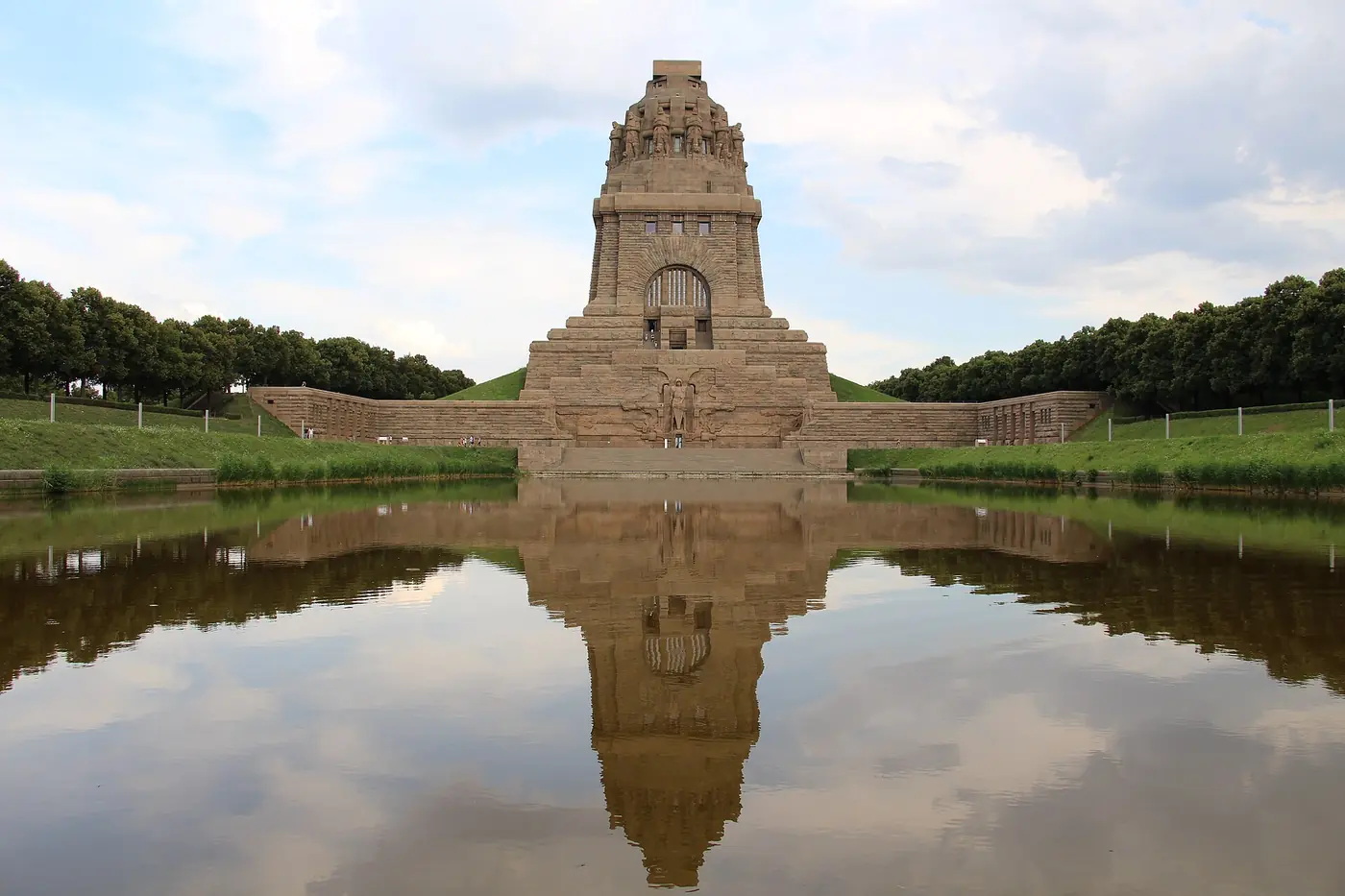 Immenso monumento di pietra a forma di torre massiccia, che si riflette in una lunga vasca bordata di prati