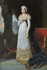 Half-length portrait of Maria Letizia Ramolino, Madame Mère, by Robert Lefèvre (c. 1813) — white Empire gown with gold embroidery at neckline and bodice, translucent blue mantle or shawl scattered with five-pointed gold stars; sheer white veil over the shoulders, gold tiara set with gems (central dark stone); pearl necklace and matching earrings, dark curls beneath the tiara; gaze to viewer, slight smile; background: stone column at left, deep red drapery — Neoclassical court painting, high point of the official "mother of the emperor" image