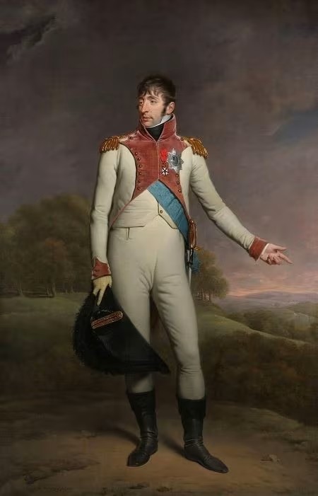 Full-length portrait of Louis Bonaparte (1778-1846), King of Holland (Koning Lodewijk), by Charles Howard Hodges (1809) — standing in court dress: light-coloured coat with high red collar and lapels richly embroidered in gold, gold-fringed epaulettes, wide light-blue sash over white waistcoat, silver star order plaque and decorations on the breast, light breeches, polished black boots; black bicorne with gold trim and red cockade held in the right hand, left hand in a formal gesture; background landscape with hills, trees and stormy cloudy sky — Neoclassical oil on canvas, state portrait of the Batavian sovereign