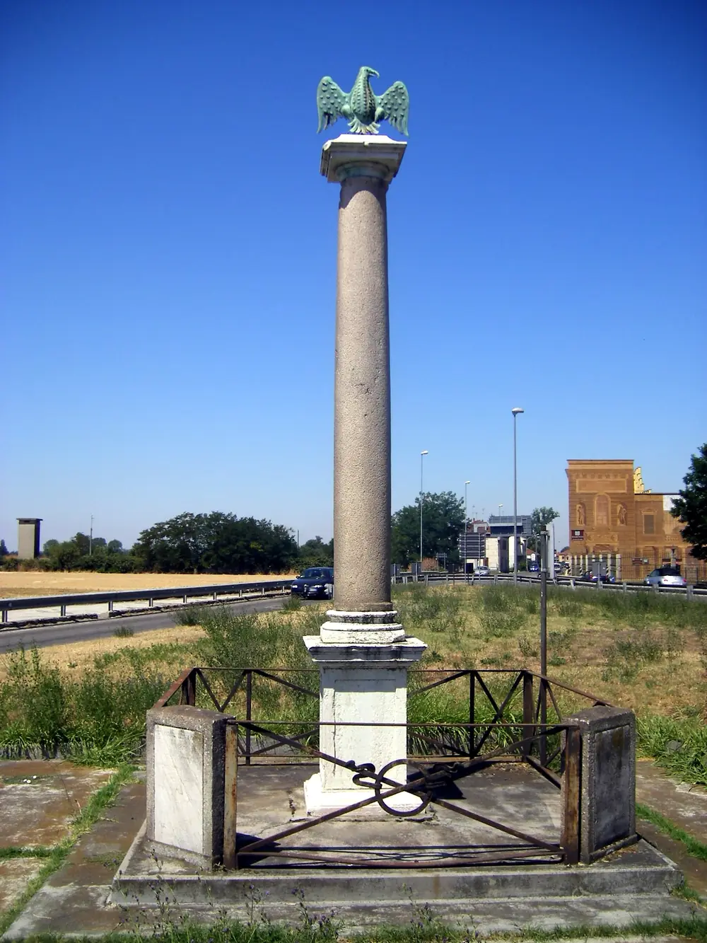Stone column on a square base surrounded by a chain, beside a road, under a blue sky