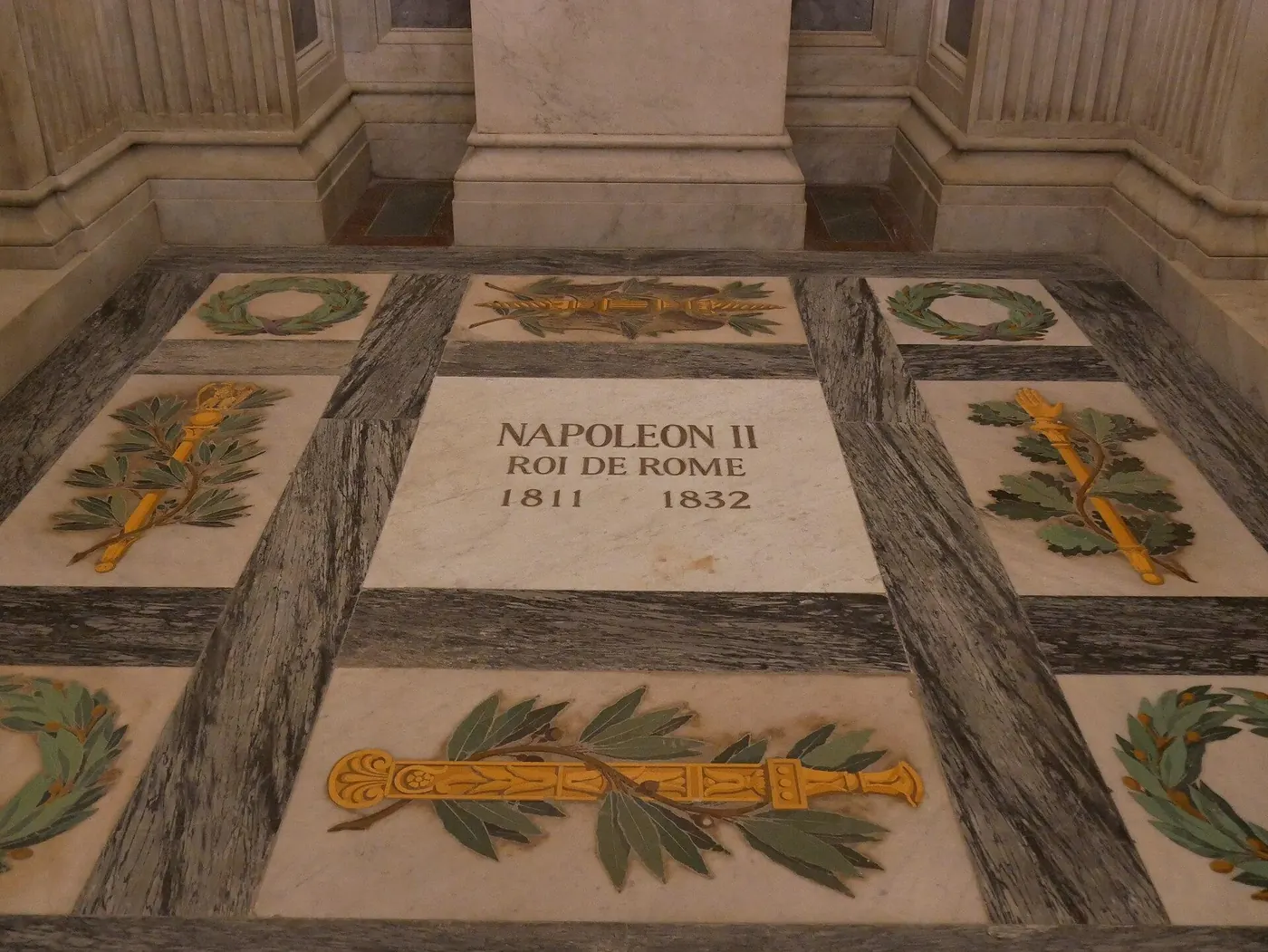 Dalle funéraire de marbre gravée « Napoléon II, roi de Rome, 1811-1832 », entourée de couronnes de laurier et de faisceaux dorés, aux Invalides
