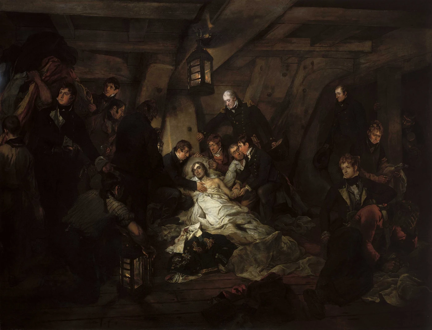 In the half-light of a lower deck, a wounded man in a white shirt lies propped up and watched over by a group of officers and seamen