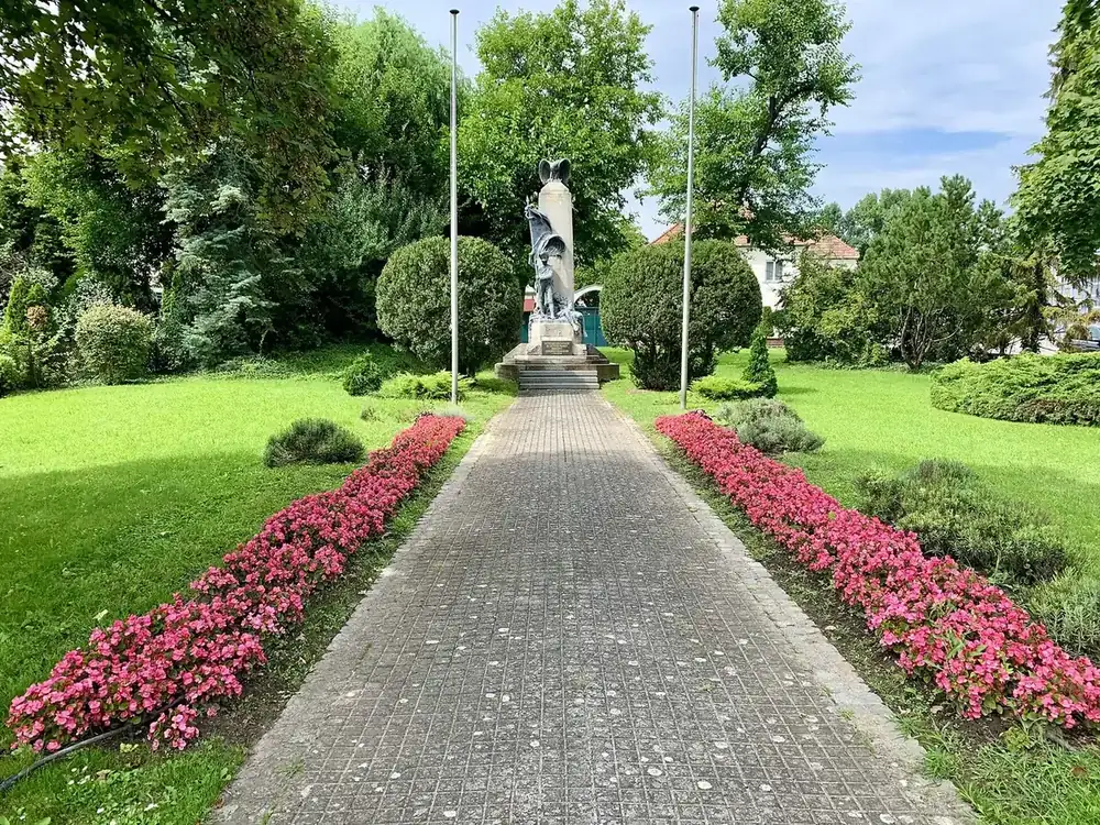 Colonne commémorative ornée d'une statue de soldat au drapeau, au bout d'une allée pavée bordée de fleurs rouges